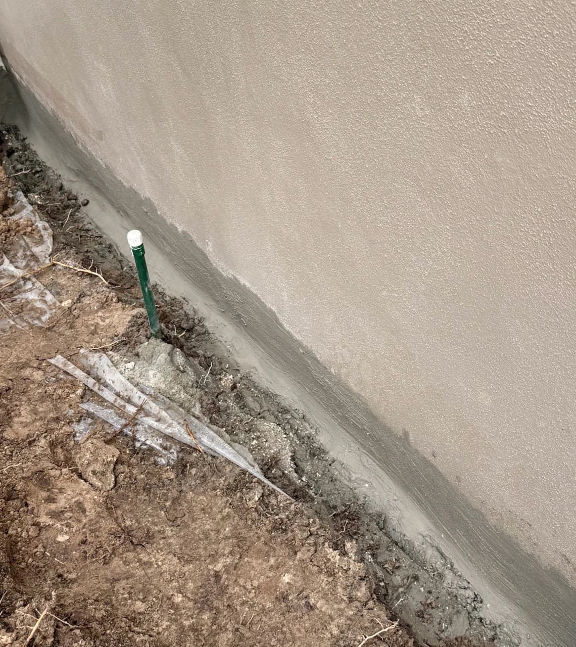 Waterproofing sealant applied at the base of an exterior concrete foundation wall with drainage pipe outlet visible
