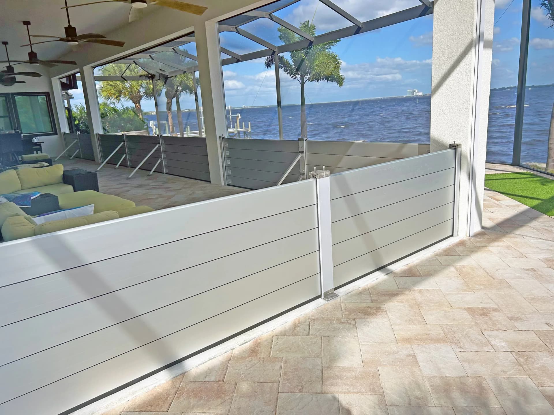 Aluminum flood barrier planks installed around a screened waterfront patio, with palm trees and open water behind Aluminum flood barrier planks installed around a screened waterfront patio, with palm trees and open water behind